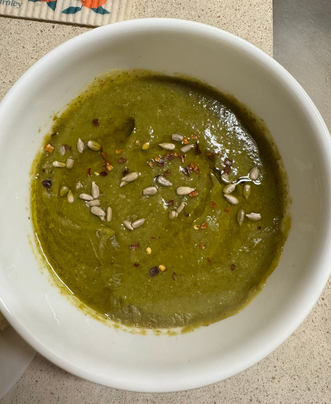 Vegan cauliflower pesto soup, creamy and herby, garnished with basil leaves and toasted pine nuts.