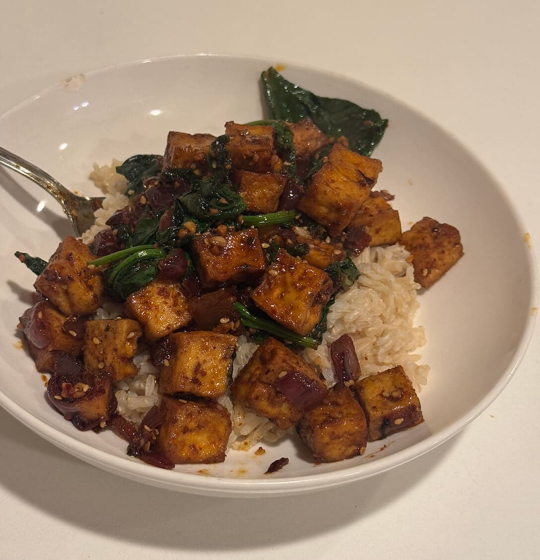 Vegan tofu and spinach stir-fry with sesame seeds, garlic, and ginger, served over rice for a quick, healthy meal.