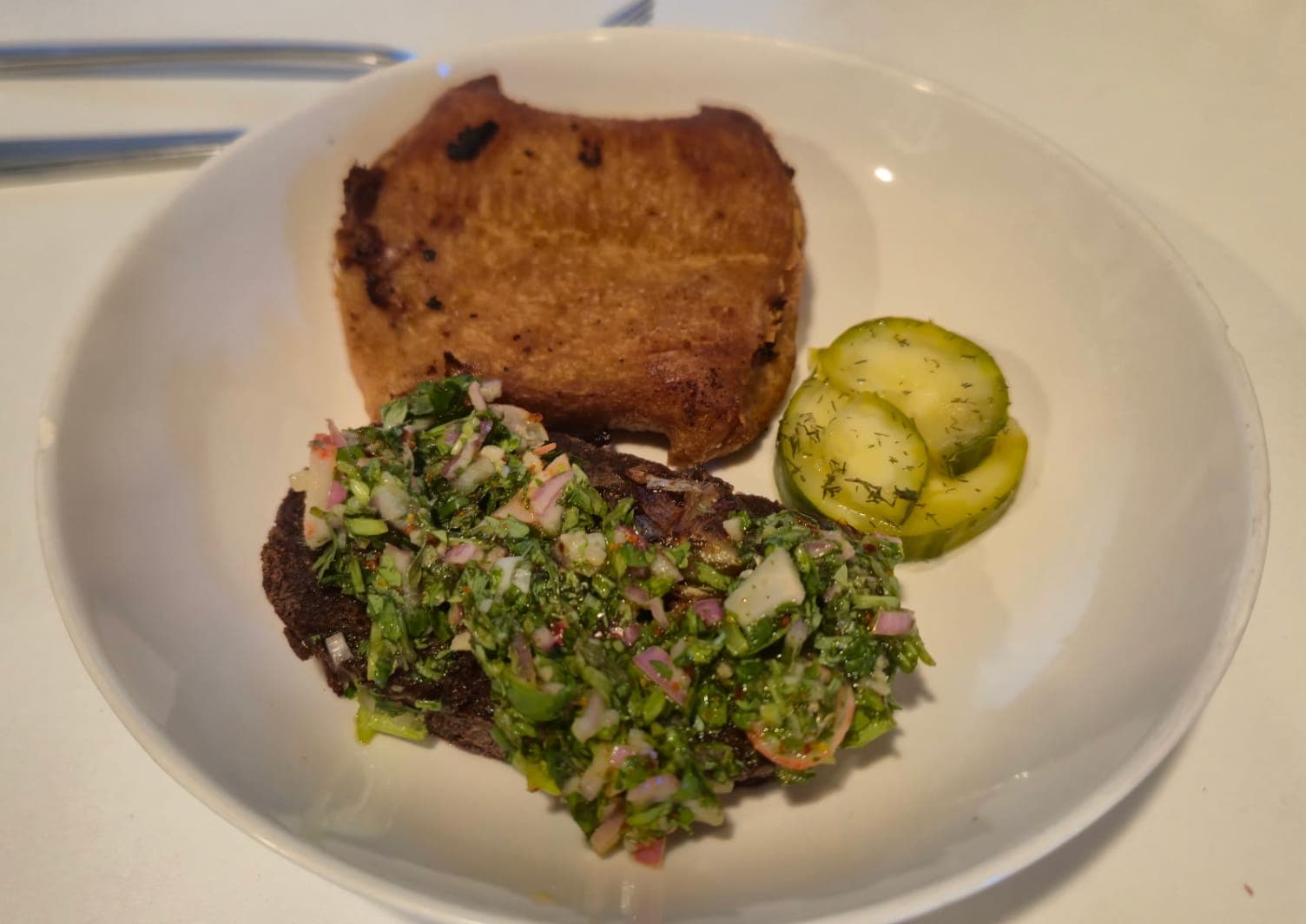 Bright green vegan cilantro radish chimichurri sauce in a small bowl, flecked with red pepper flakes and chopped radish, served over grilled vegan steak.